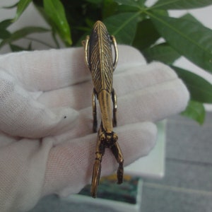 May include: A gold-coloured metal praying mantis figurine. The mantis is standing on its hind legs with its front legs raised in a praying position.