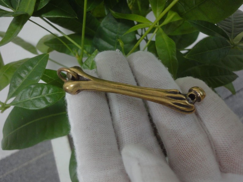 May include: A gold-colored bone-shaped pendant with a ring at the top for attaching to a chain or cord.