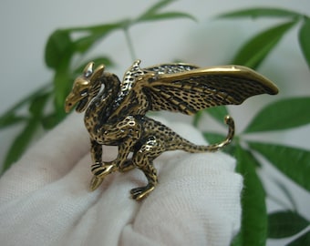 May include: A small, gold-colored dragon figurine with wings outstretched. The dragon has a textured surface and a detailed design.