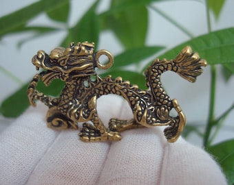 Puede incluir: Un colgante de metal dorado en forma de dragón con detalles intrincados. El dragón está enroscado con su cola envuelta alrededor de su cuerpo. El colgante tiene un bucle en la parte superior para sujetarlo a una cadena o cordón.