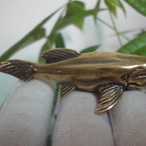 Puede incluir: Una pequeña escultura de bronce detallada de un pez con un hocico largo y puntiagudo. El pez está representado en un estilo realista, con aletas y escamas visibles.