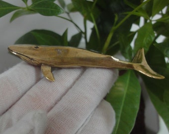 May include: A small, gold-colored metal whale figurine. The whale is detailed with a fin and tail.