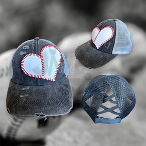 May include: A black distressed baseball cap with a white heart-shaped patch featuring a baseball stitch design. The cap has a mesh back with a criss-cross design.