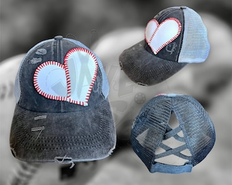 May include: A black distressed baseball cap with a white heart-shaped patch featuring a baseball stitch design. The cap has a mesh back with a criss-cross design.