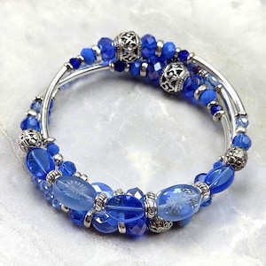 May include: A blue beaded bracelet with silver accents. The bracelet features various shades of blue beads, including faceted and oval shapes, interspersed with silver-colored metal beads. The design is multi-strand, creating a layered effect. The bracelet is likely for fashion or jewelry.