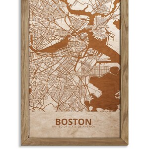 May include: A wood-mounted map of Boston, Massachusetts, with the city's streets and neighborhoods outlined in brown. The map is framed in a light brown wood frame. The text "BOSTON" and "UNITED STATES OF AMERICA" is printed below the map.