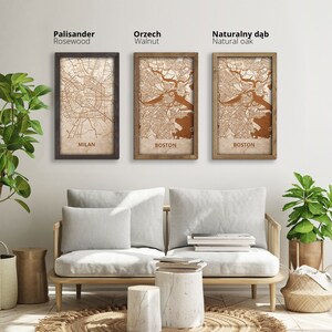 May include: Three framed city maps with different wood finishes: rosewood, walnut, and natural oak. The maps show the city layouts of Milan, Boston, and Boston. The frames are displayed on a white wall above a light gray couch with white pillows.
