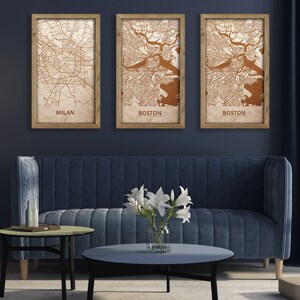 May include: Three framed maps of Milan and Boston, with a brown background and copper-colored lines, hanging on a dark blue wall above a blue velvet sofa and two coffee tables.