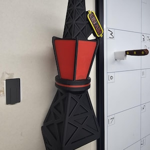 Puede incluir: Un im&aacute;n negro y rojo con forma de torre de radio con un letrero amarillo de "ON AIR". El im&aacute;n est&aacute; adherido a una pared blanca. La torre tiene un dise&ntilde;o geom&eacute;trico y una secci&oacute;n central roja.