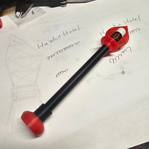 Könnte beinhalten: Ein schwarz-rotes 3D-gedrucktes Modell eines Hotelgebäudes mit dem Text "Hazbin Hotel" auf einem weißen Blatt Papier.