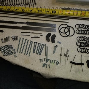 May include: A collection of metal parts for a DIY project, including springs, rods, screws, nuts, and washers. There are also several black rubber rings and a few small metal pieces.