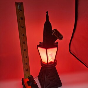 Puede incluir: L&aacute;mpara negra con forma de torre con un brillo rojo, con un letrero de "ON AIR". La l&aacute;mpara mide aproximadamente 18 cm de alto. La base tiene un dise&ntilde;o geom&eacute;trico. Una cinta m&eacute;trica est&aacute; al lado de la l&aacute;mpara.