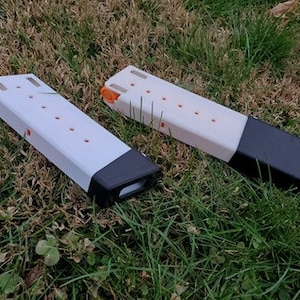 May include: Two white plastic magazine holders with black end caps. The holders have orange accents and multiple holes.