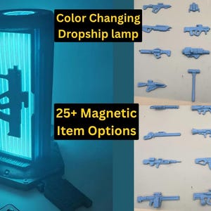 May include: A cylindrical color-changing lamp emitting a bright blue light with a silhouette of a rifle on the front. The text reads Color Changing Dropship lamp and 25+ Magnetic Item Options. A collection of various small gray magnetic weapon accessories.