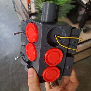 May include: A 3D printed traffic light model with four red circular lights. The model is gray with a yellow wire attached to the top.