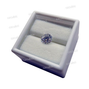 May include: A clear oval-shaped gemstone in a white velvet-lined jewelry box.
