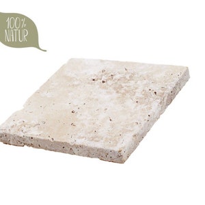 May include: A square, light beige travertine stone tile with a porous, textured surface. The tile features natural pits and variations in its off-white and tan coloring. A leaf-shaped graphic in the upper left corner contains the text 100% NATUR.