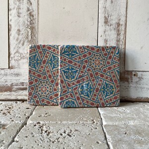 Puede incluir: Dos azulejos cuadrados de cer&aacute;mica con un patr&oacute;n geom&eacute;trico en tonos de azul, rojo y amarillo. Los azulejos tienen un aspecto desgastado y vintage.