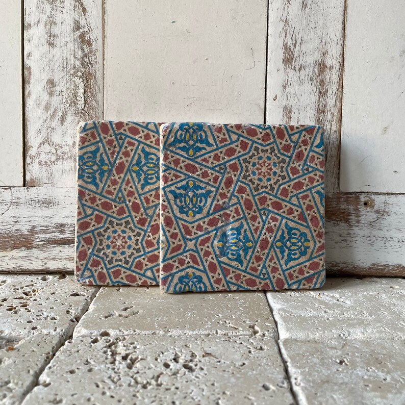 Puede incluir: Dos azulejos cuadrados de cer&aacute;mica con un patr&oacute;n geom&eacute;trico en tonos de azul, rojo y amarillo. Los azulejos tienen un aspecto desgastado y vintage.