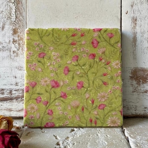 Könnte beinhalten: Ein quadratischer grüner Untersetzer mit einem Blumenmuster. Das Muster zeigt rosa Blüten und grüne Blätter auf einem hellgrünen Hintergrund.