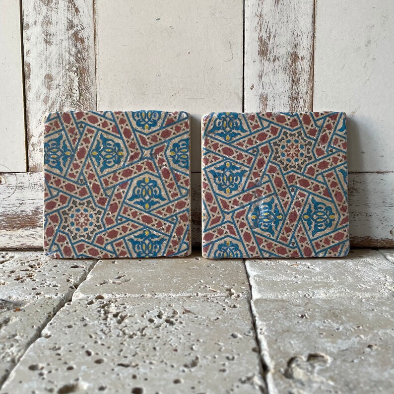 Puede incluir: Dos azulejos cuadrados de cer&aacute;mica con un patr&oacute;n geom&eacute;trico en tonos de azul, rojo y amarillo. Los azulejos tienen un aspecto desgastado y vintage.