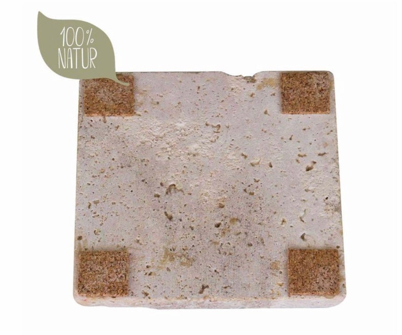 May include: A square, porous, light beige stone coaster with a textured, uneven surface. Four small, brown, square cork pads are attached to the corners of the underside. A light green leaf-shaped graphic in the top left corner displays the text 100% NATUR.