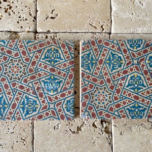 Puede incluir: Dos azulejos cuadrados de cer&aacute;mica con un patr&oacute;n geom&eacute;trico en tonos rojos, azules, amarillos y negros. El patr&oacute;n es intrincado y presenta estrellas, diamantes y otras formas.