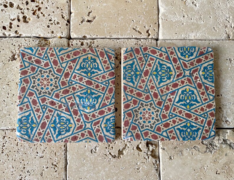 Puede incluir: Dos azulejos cuadrados de cer&aacute;mica con un patr&oacute;n geom&eacute;trico en tonos rojos, azules, amarillos y negros. El patr&oacute;n es intrincado y presenta estrellas, diamantes y otras formas.