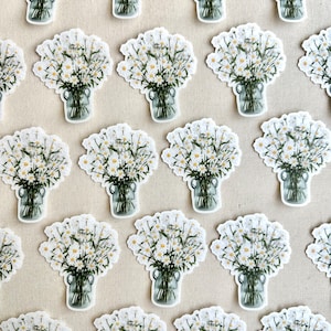 May include: A collection of white daisy bouquets in glass jars, arranged in a grid pattern on a beige surface. The daisies are white with green stems and leaves.