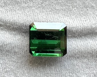 May include: A vibrant green emerald cut gemstone with a rectangular shape.