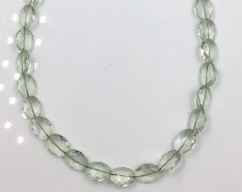 May include: A strand of light green oval-shaped gemstone beads with a silver clasp.