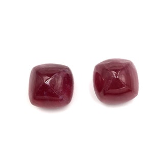 Op de afbeelding: Twee vierkante edelstenen in donkerrood met een facetgeslepen vorm.