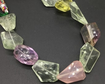 Può includere: Una collana di perle di pietre preziose sfaccettate in tonalità di verde, rosa e viola. Le perle sono infilate su un cordoncino con un fiocco colorato.