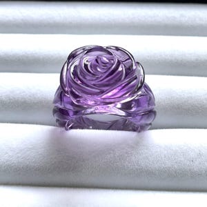 Pode incluir: Um anel de ametista roxa esculpido em forma de rosa.