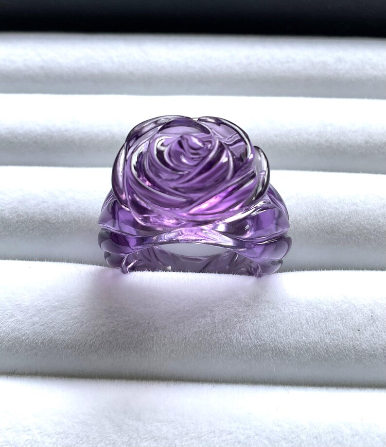 Pode incluir: Um anel de ametista roxa esculpido em forma de rosa.