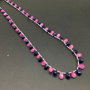 May include: A strand of pink and blue gemstone beads, strung on a silver thread. The beads are teardrop shaped and have a faceted finish.