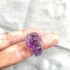 Pode incluir: Um anel de rosa de ametista roxo. O anel &eacute; esculpido em uma &uacute;nica pe&ccedil;a de ametista e apresenta um design de rosa detalhado.