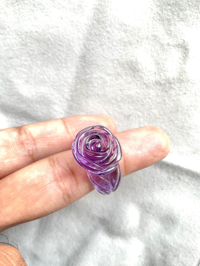 Pode incluir: Um anel de rosa de ametista roxo. O anel &eacute; esculpido em uma &uacute;nica pe&ccedil;a de ametista e apresenta um design de rosa detalhado.