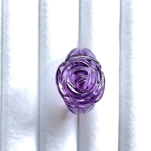 Pode incluir: Um anel de vidro roxo em forma de rosa. A rosa &eacute; esculpida em detalhe e tem um acabamento brilhante.