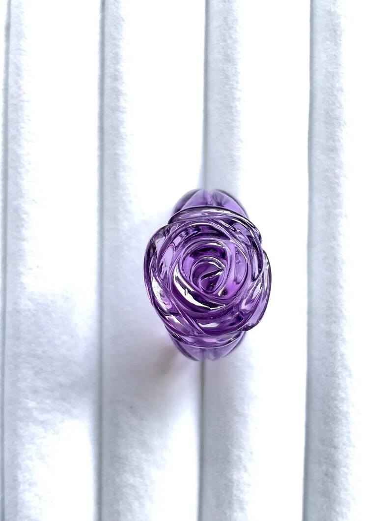 Pode incluir: Um anel de vidro roxo em forma de rosa. A rosa &eacute; esculpida em detalhe e tem um acabamento brilhante.