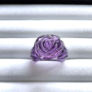Pode incluir: Um anel de vidro rosa roxo. O anel &eacute; feito de vidro transparente com um tom roxo e tem a forma de uma rosa.