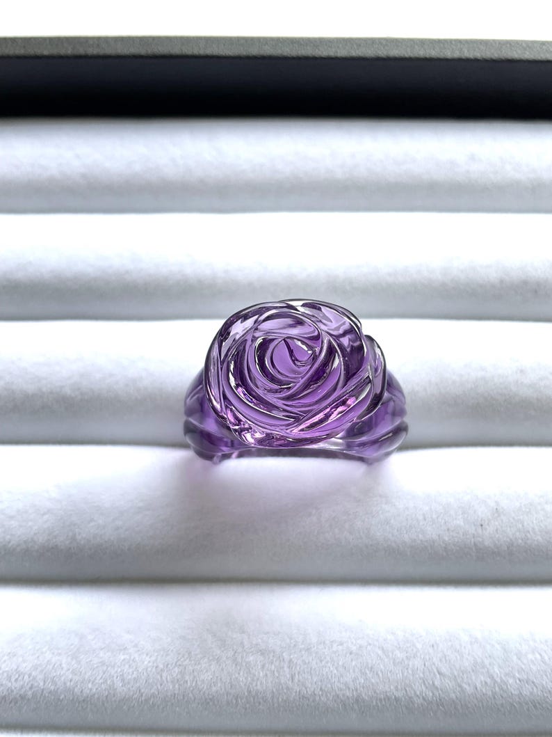 Pode incluir: Um anel de vidro rosa roxo. O anel &eacute; feito de vidro transparente com um tom roxo e tem a forma de uma rosa.