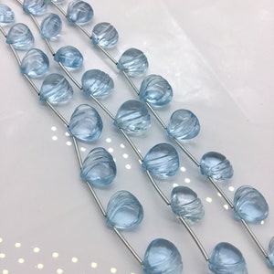 May include: Three strands of light blue gemstone beads, each bead is faceted and shaped like a teardrop. The beads are strung on silver wire.