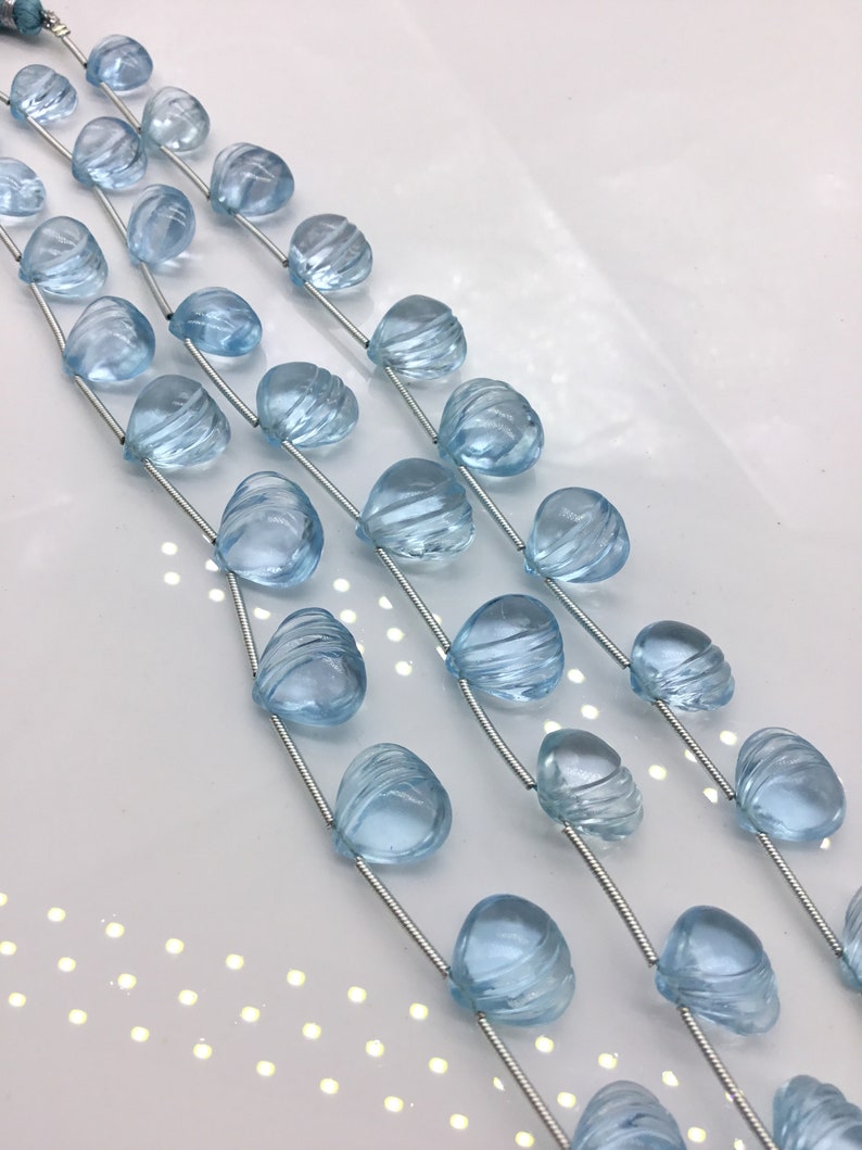 May include: Three strands of light blue gemstone beads, each bead is faceted and shaped like a teardrop. The beads are strung on silver wire.