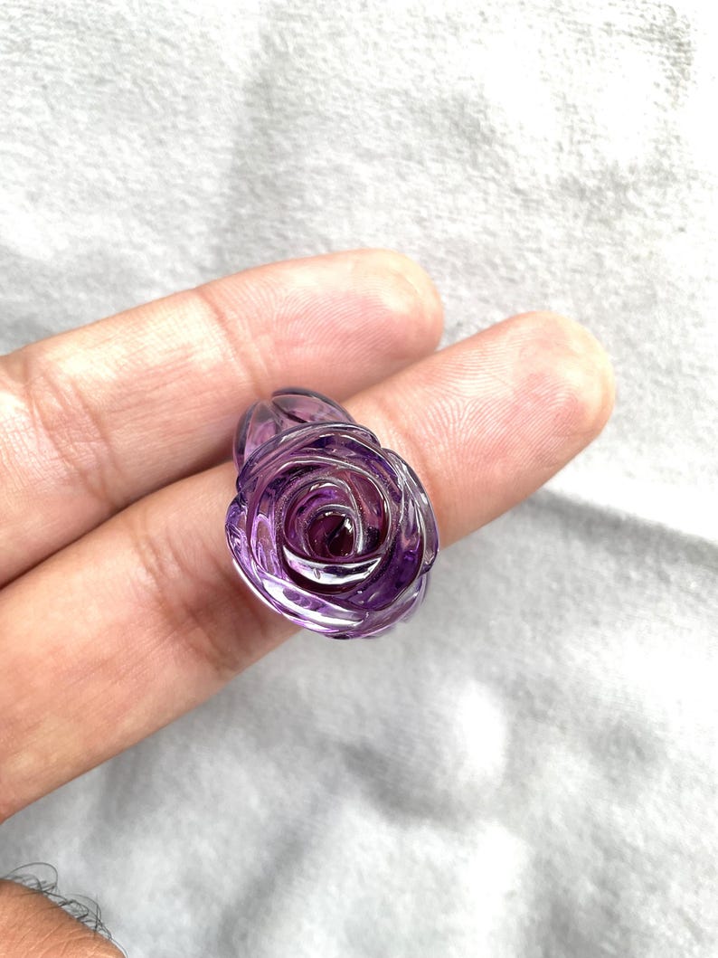 Pode incluir: Uma ametista roxa esculpida em forma de rosa. A rosa &eacute; detalhada e intrincada.