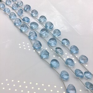 May include: A strand of light blue gemstone beads, each bead is faceted and has a unique shape. The beads are strung on a silver wire and are ready to be used for jewelry making.