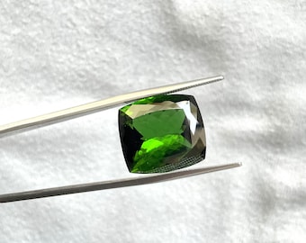 May include: A vibrant green gemstone with a square cushion cut, held by tweezers against a white background.