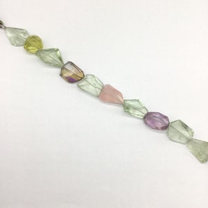 May include: A strand of faceted gemstone beads in various shades of green, pink, and purple. The beads are strung on a clear thread and are arranged in a staggered pattern.