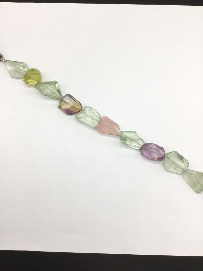 May include: A strand of faceted gemstone beads in various shades of green, pink, and purple. The beads are strung on a clear thread and are arranged in a staggered pattern.