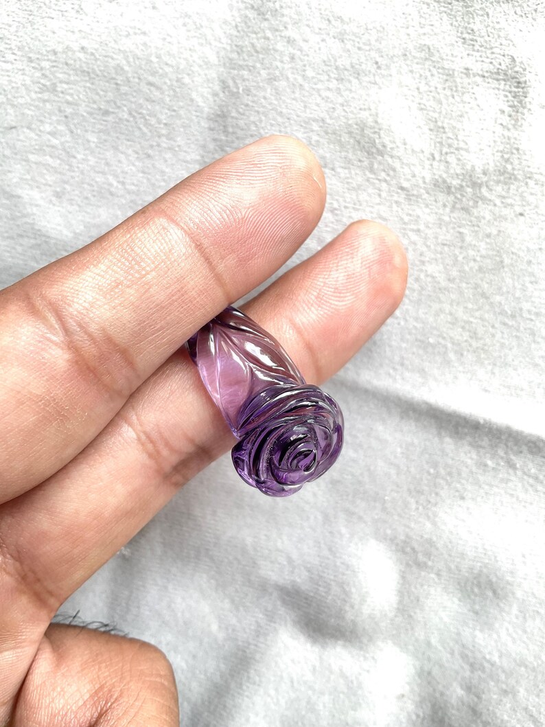 Pode incluir: Um anel de ametista roxa esculpido em forma de rosa.